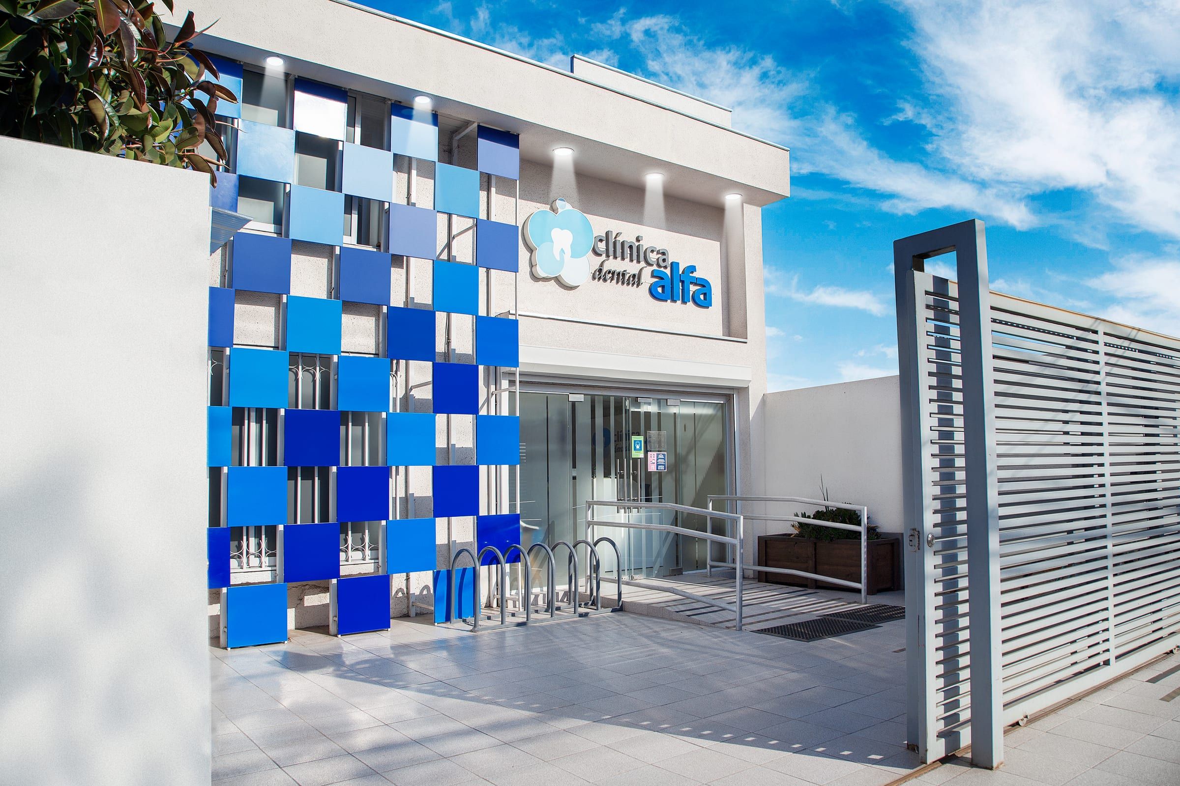 Fachada de Clínica Dental Alfa en Av. Tres Poniente 0868, Maipú: revestimiento de cuadrados azules, entrada de vidrio y rampa de acceso.
